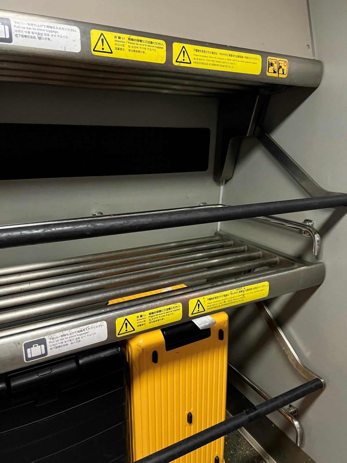 Yellow suitcase on metal luggage rack with warning labels.