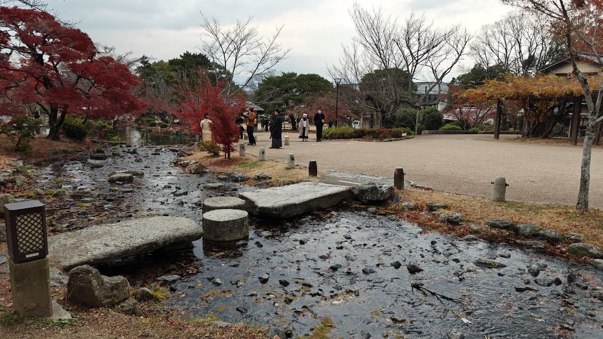 Autumn park with stream, red trees, and people strolling
