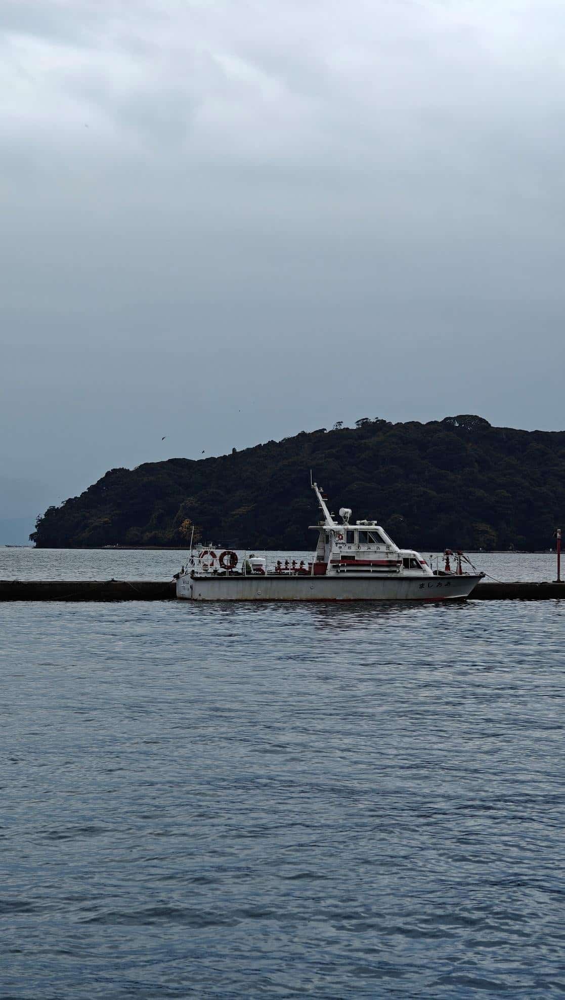 Boat near island under cloudy sky on calm waters
