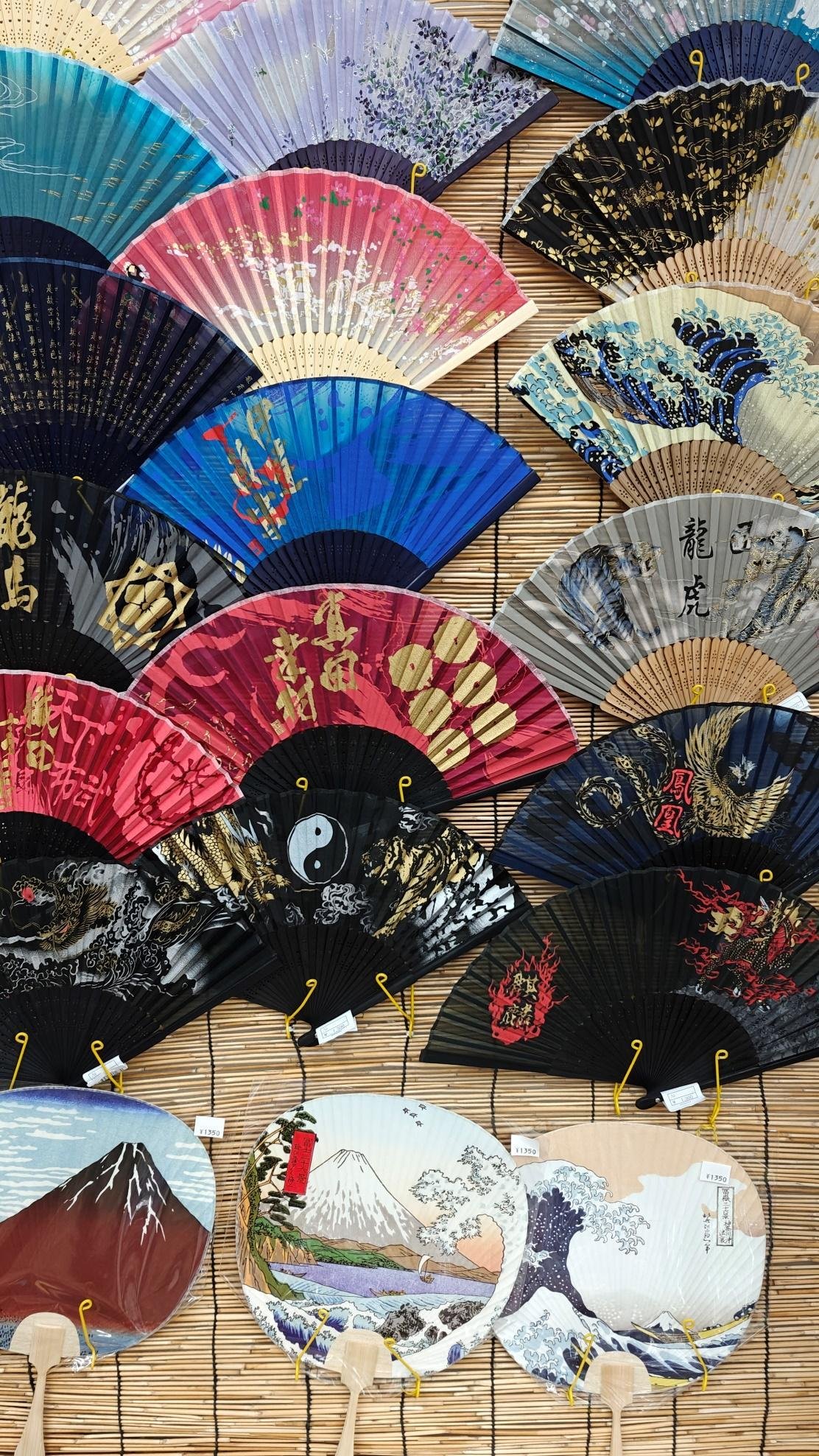 Colorful Japanese fans with intricate designs on bamboo mat
