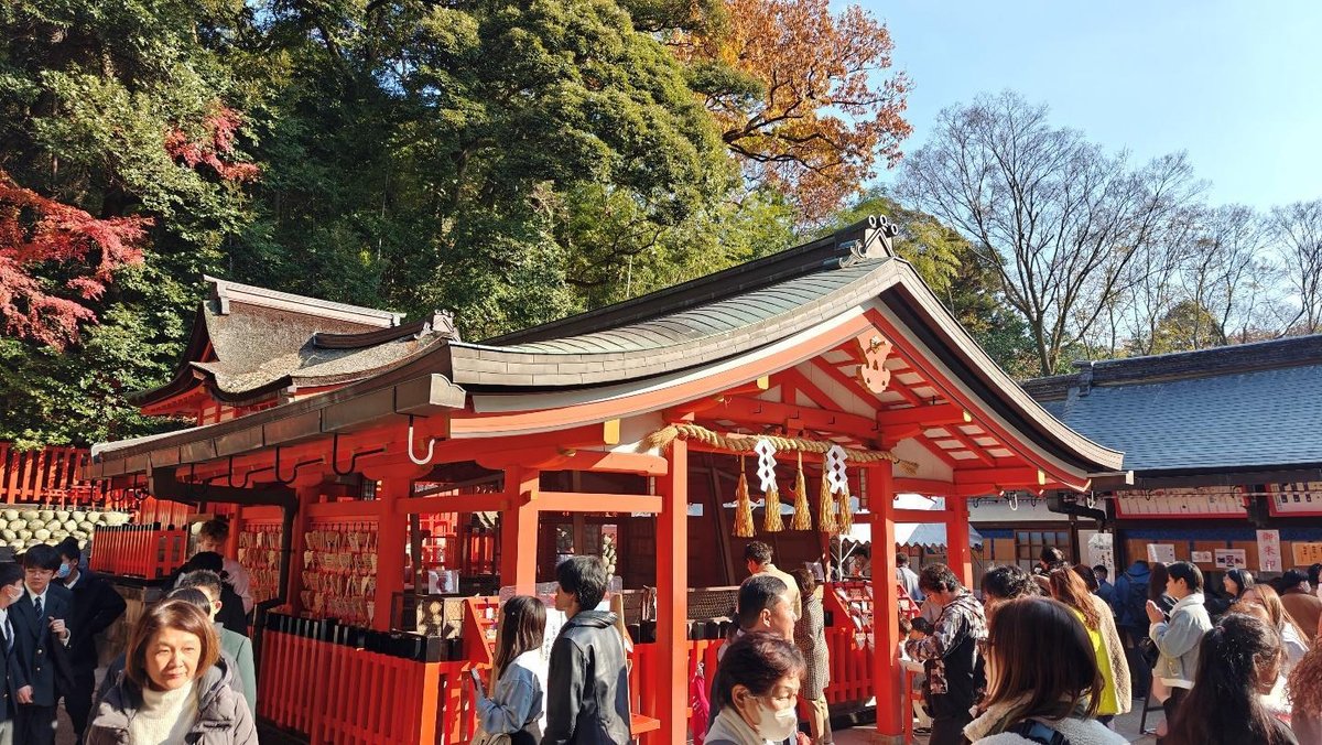 Crowd at a vibrant red Shinto shrine under autumn trees