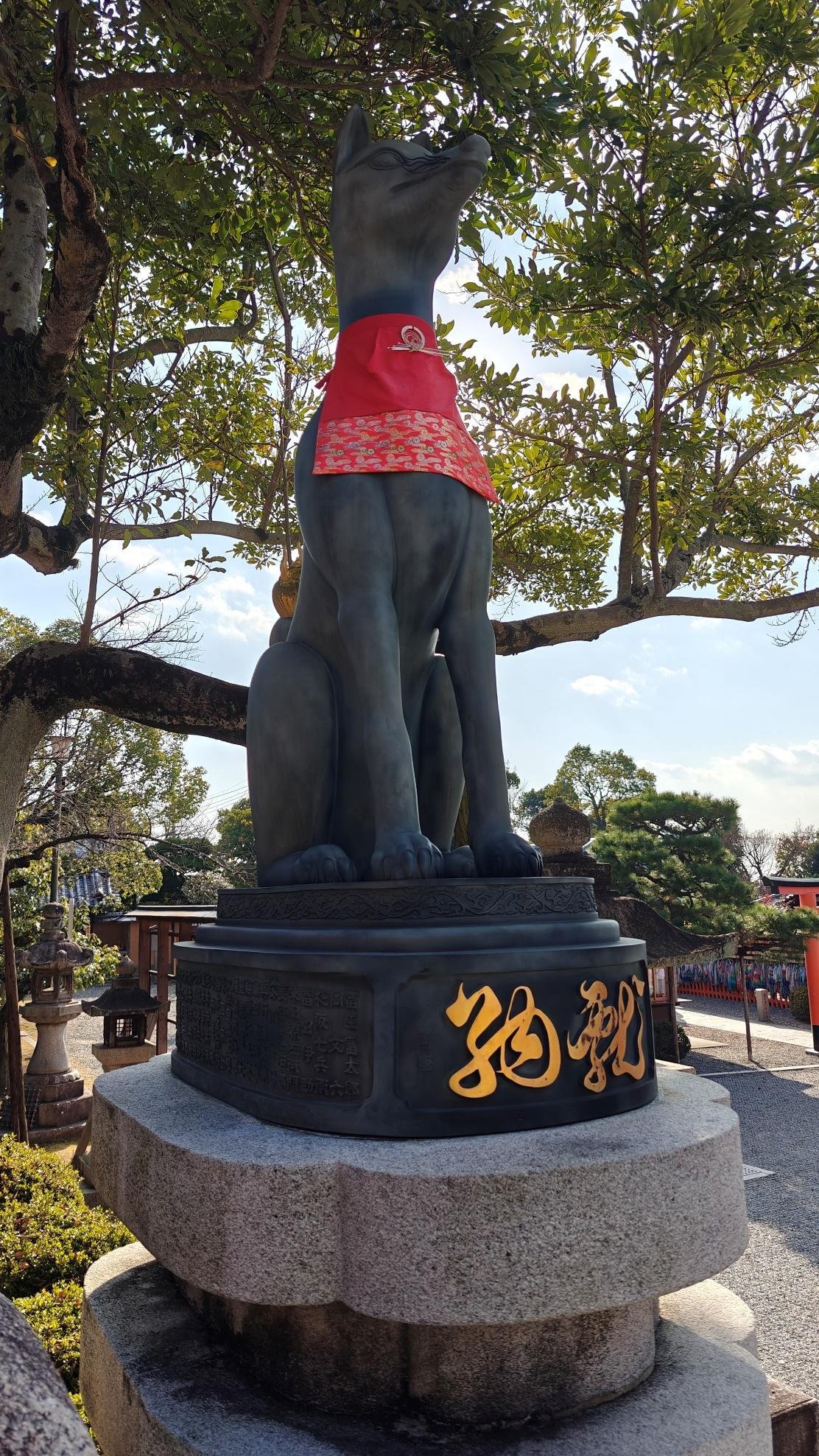 Fox statue with red bib under leafy trees
