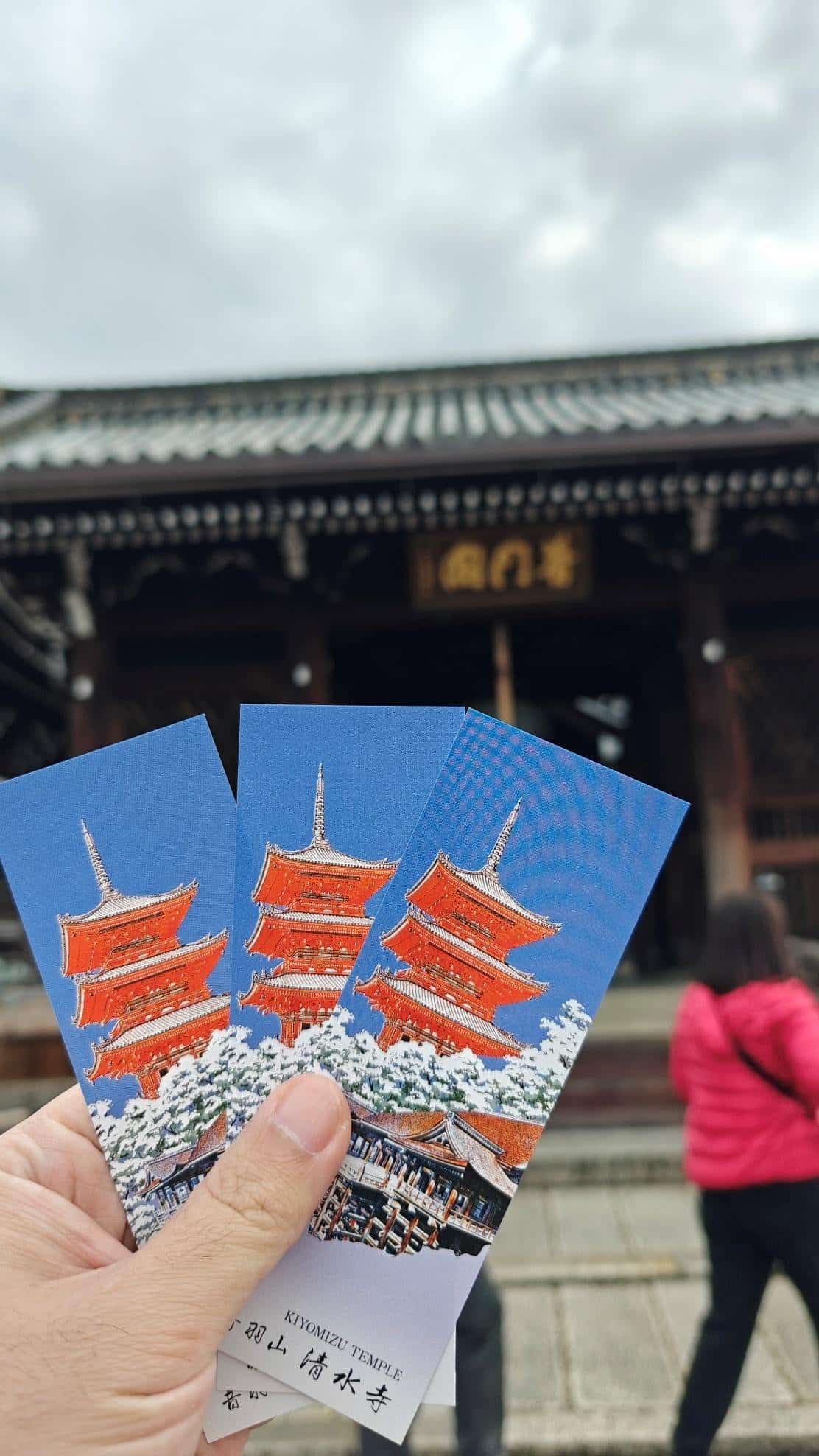 Hand holding Kiyomizu Temple tickets, blurred historic building behind