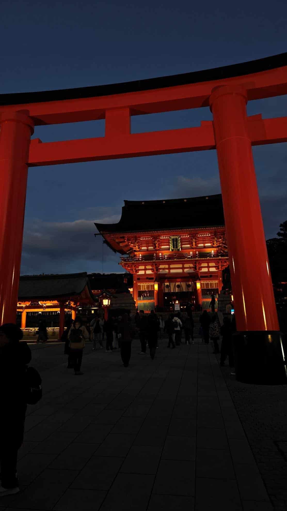 Illuminated red shrine gate at twilight with visitors