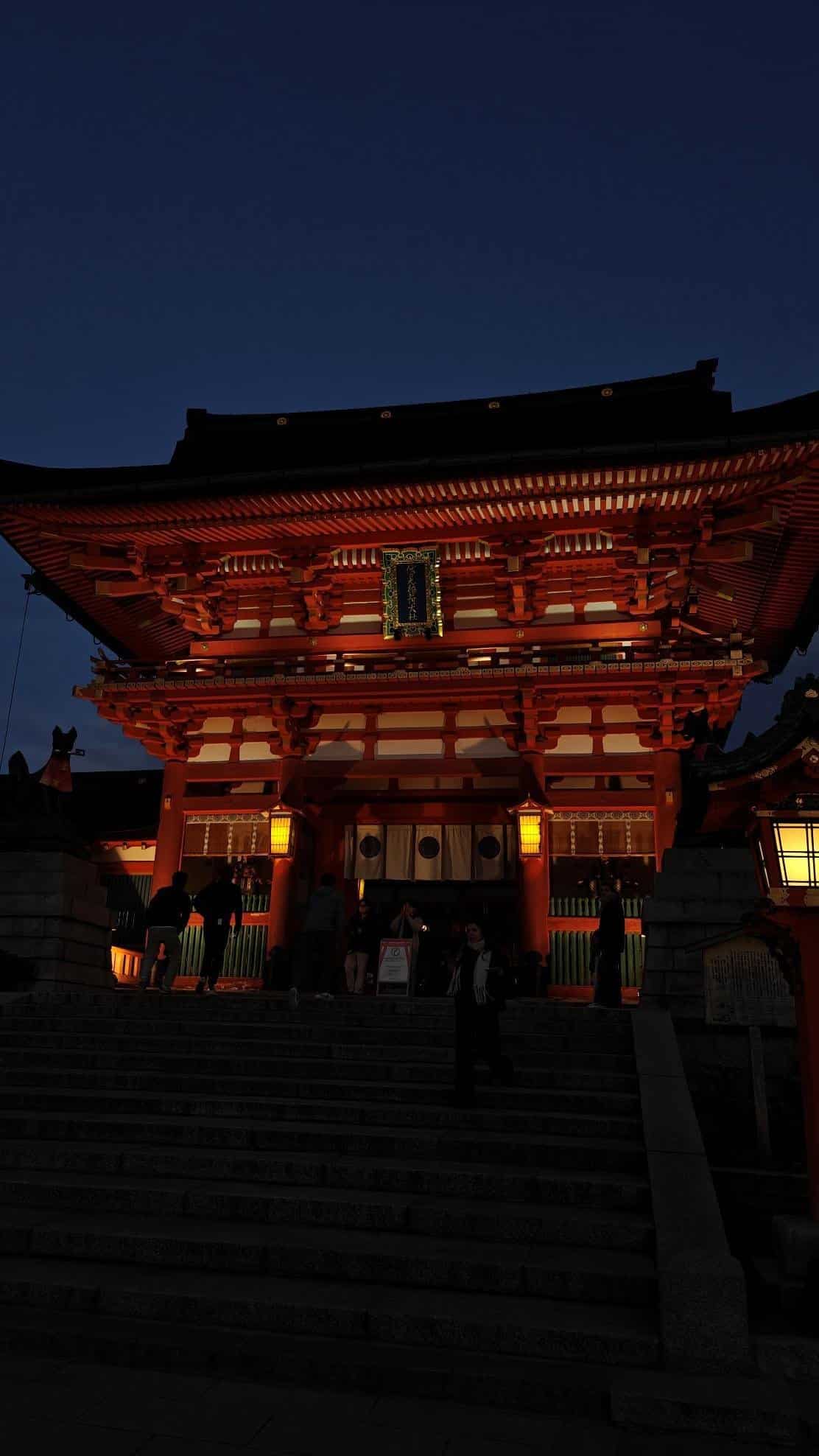 Illuminated temple gate at dusk with people on stone steps