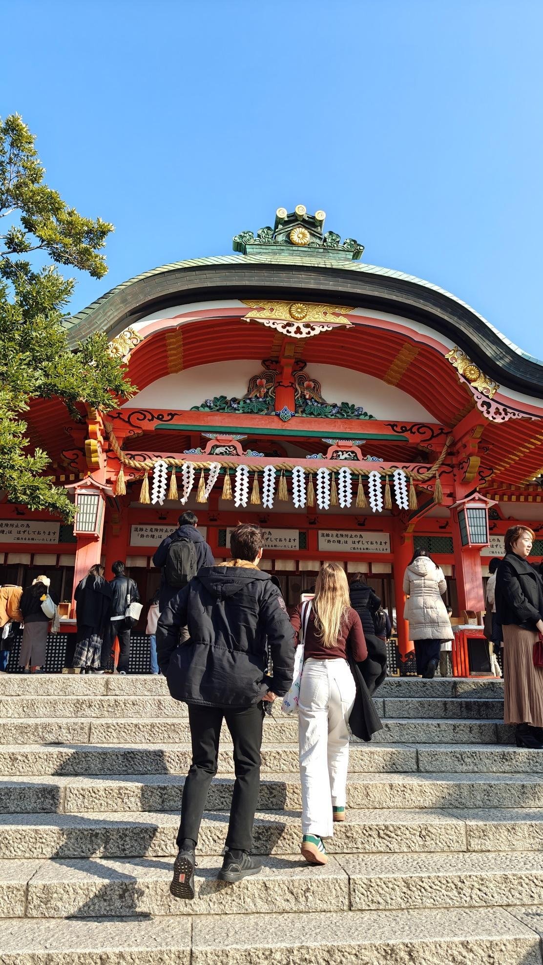 People ascending steps to colorful Japanese shrine under blue sky