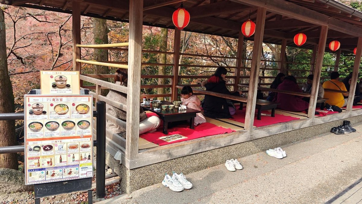 People dining in outdoor pavilion with autumn trees