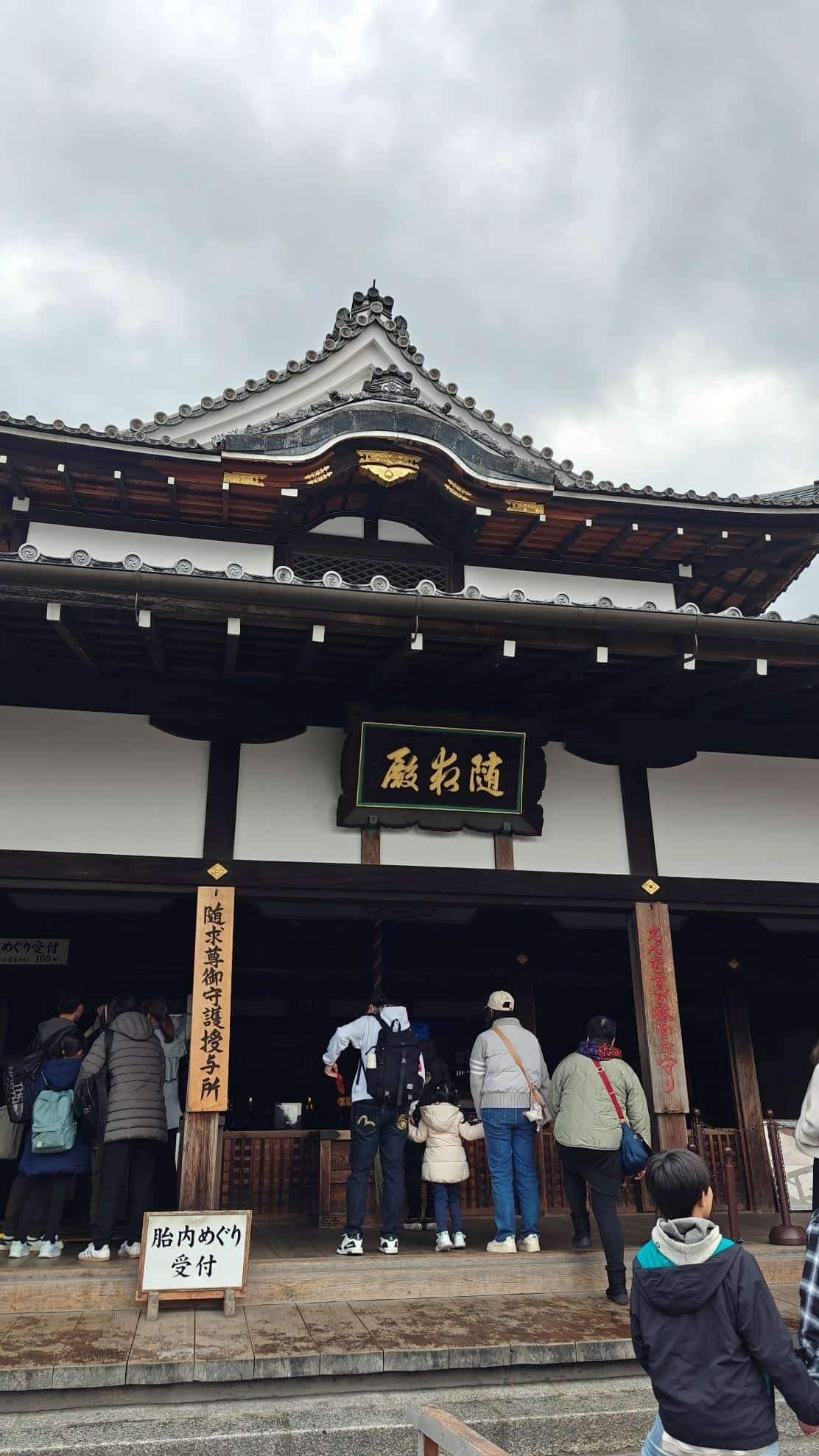 People entering traditional wooden temple under cloudy sky