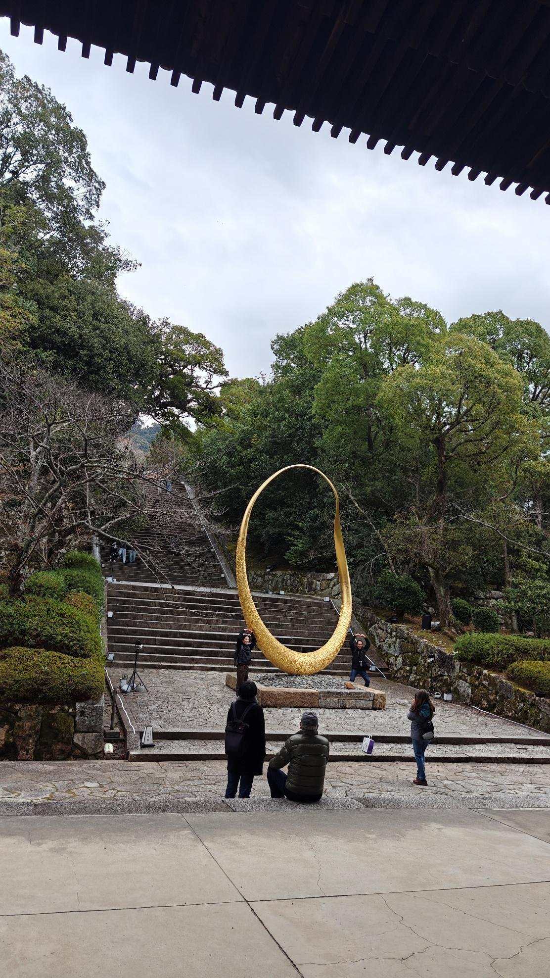 People near gold sculpture on steps amid lush greenery