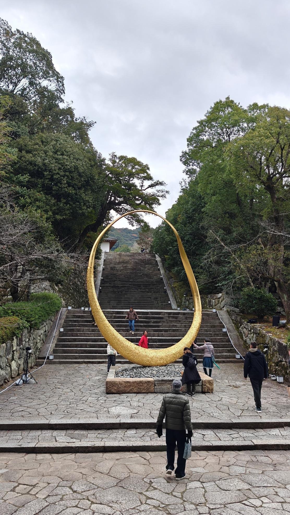 People walking near a golden sculpture on stone steps