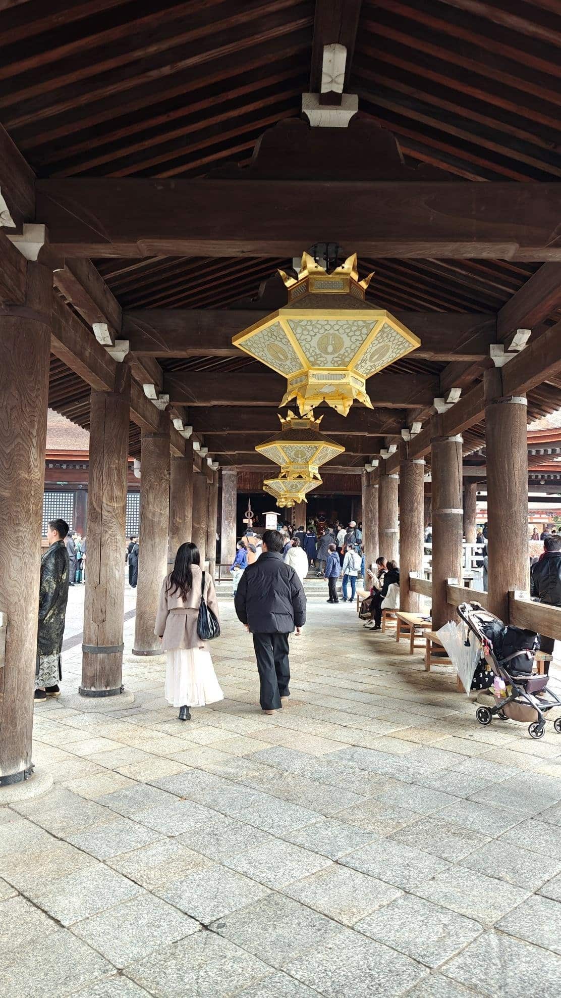 People walking under ornate wooden temple corridor