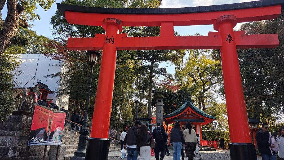 People walking under vibrant red torii gate in lush temple garden