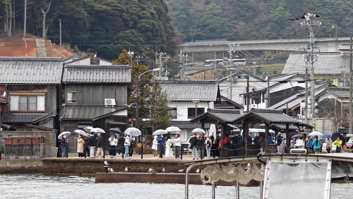 People with umbrellas near wooden buildings by water