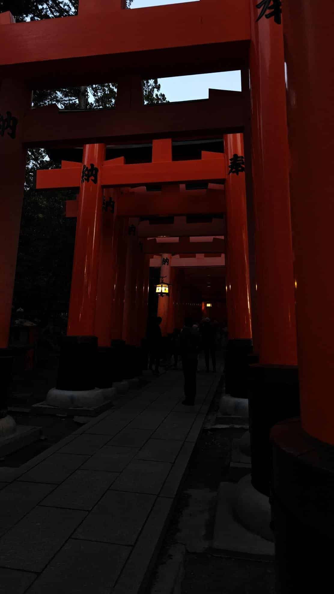 Red torii gates at dusk with silhouettes of people walking
