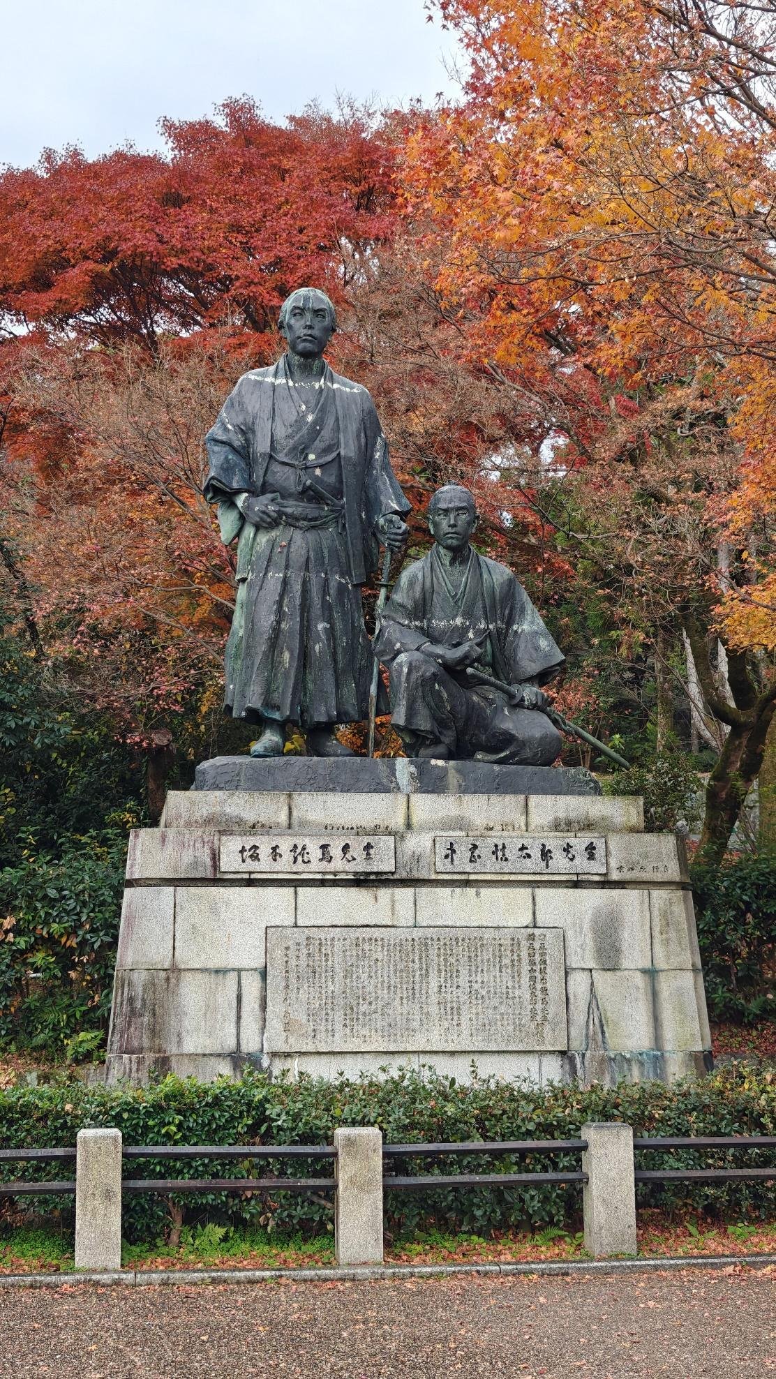Statue of two figures with autumn foliage background