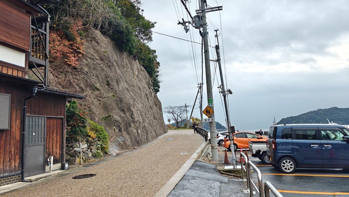 Steep hillside road with parked cars and sea view