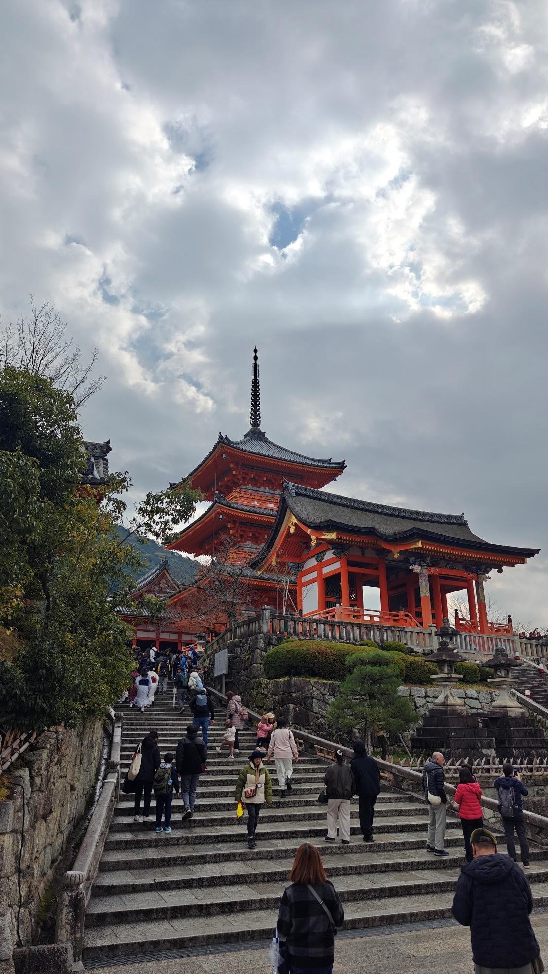 Tourists ascending stairs to vibrant traditional temple under cloudy sky
