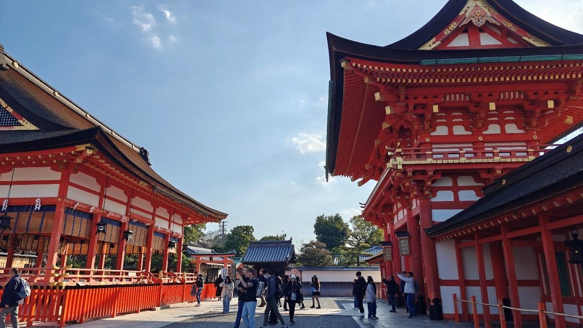 Tourists exploring vibrant red Japanese temple, clear sky