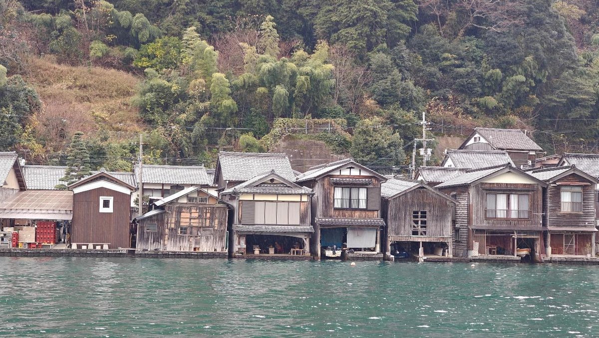 Traditional wooden boathouses along a forested waterfront