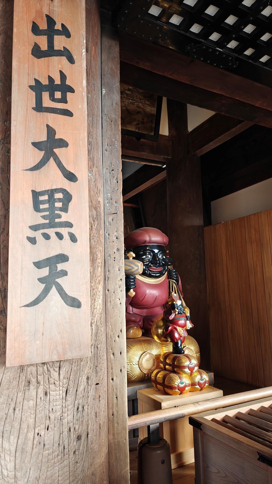 Wooden statue with ornate details next to Japanese text sign