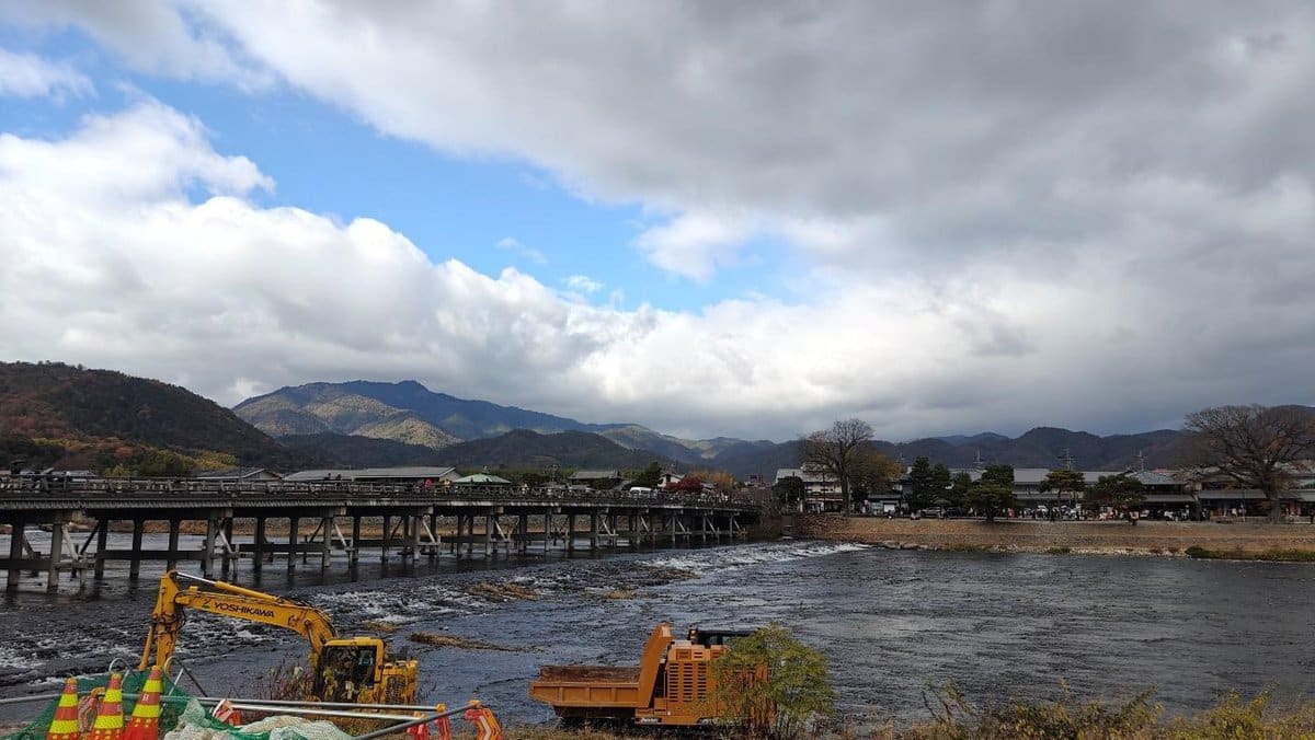 Bridge over river with mountains under cloudy sky