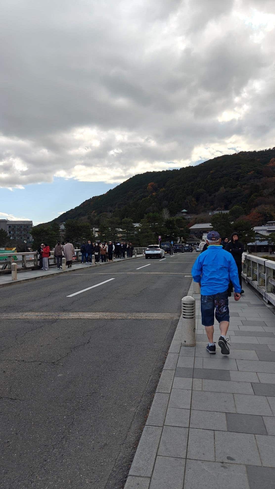 Crowded bridge under cloudy sky with mountain backdrop