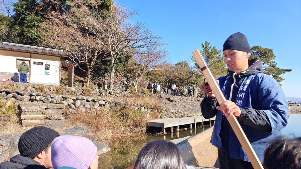 Guide in traditional attire steering boat by scenic riverside