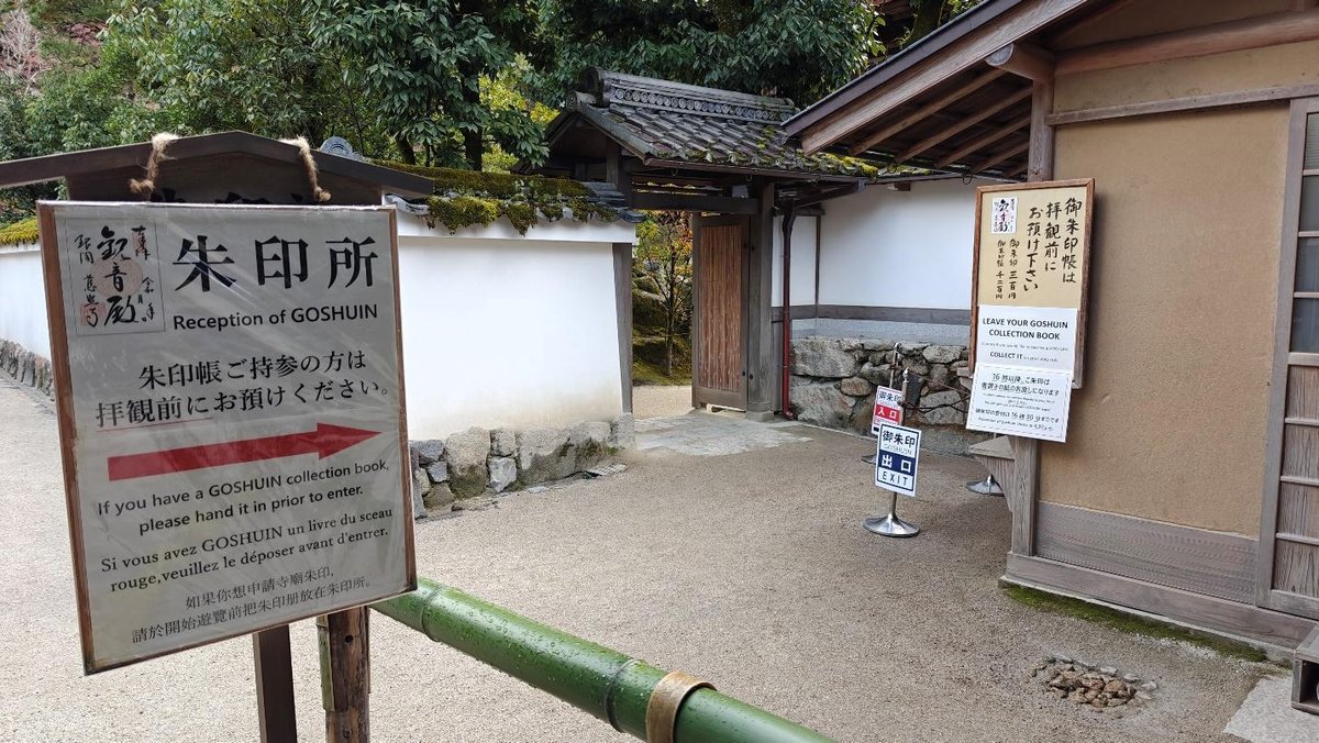 Japanese temple entrance with sign and lush greenery