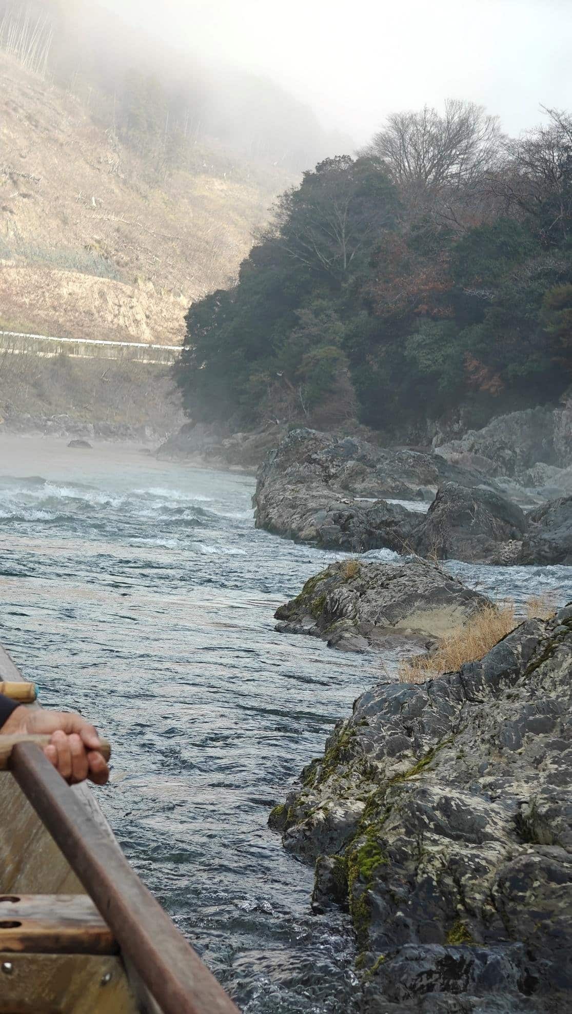 Misty river with rocky shore and boat passenger's hand