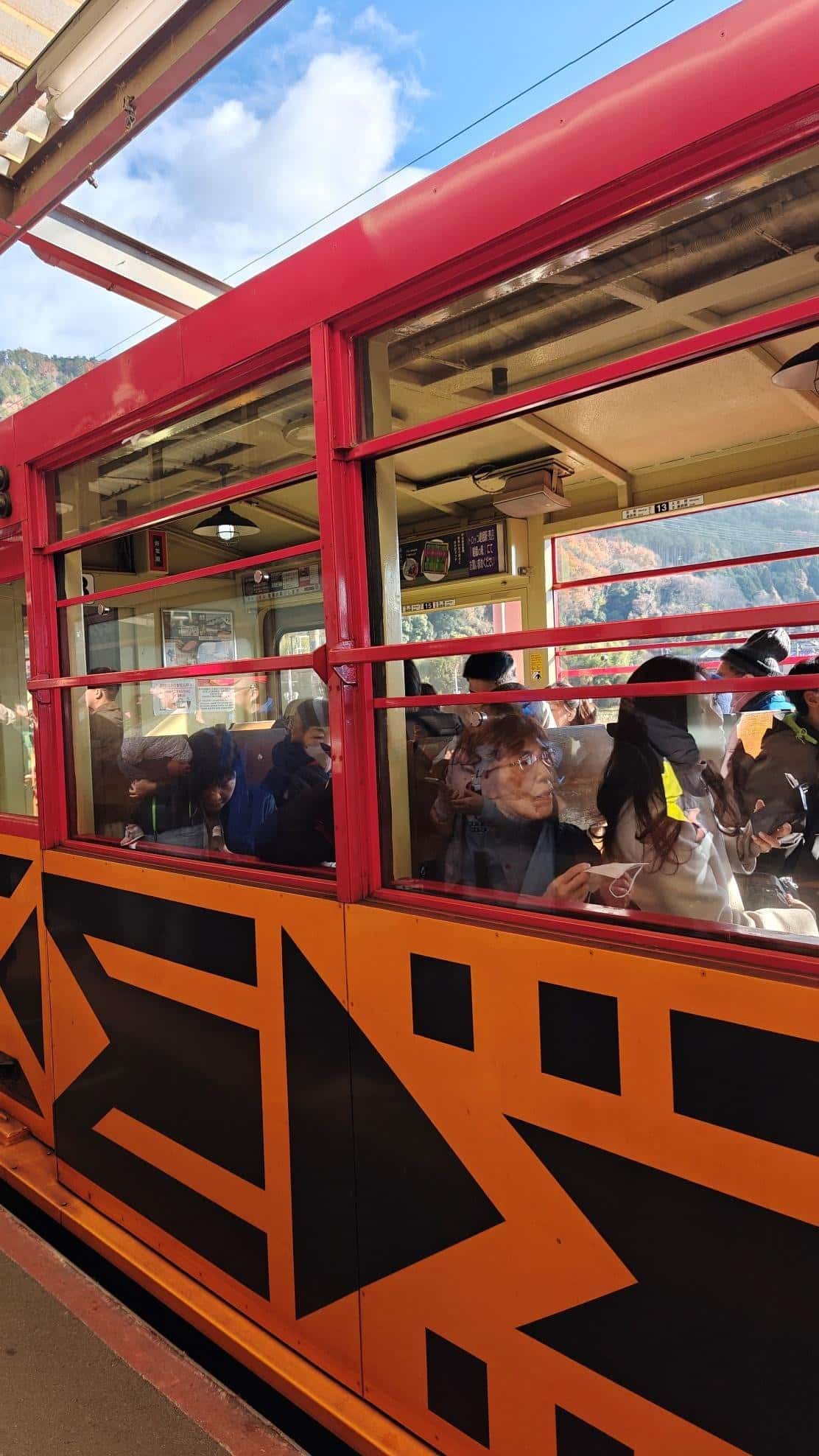Passengers inside red and orange train with clear sky view