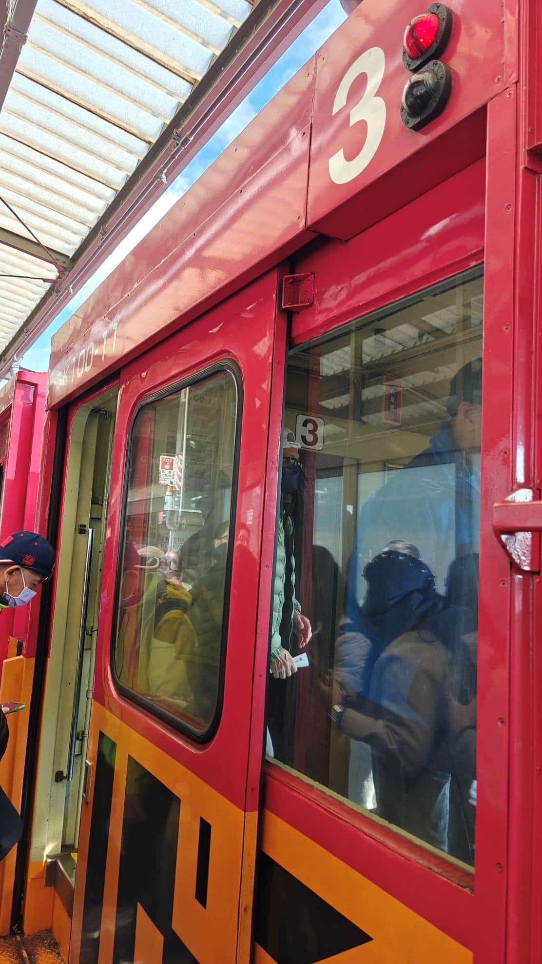 People boarding a red train at a station with glass windows