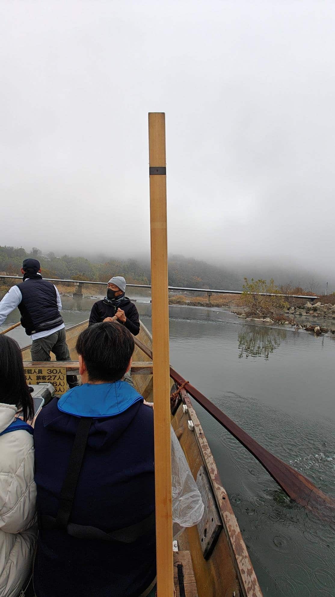 People boating on misty river with foggy hills