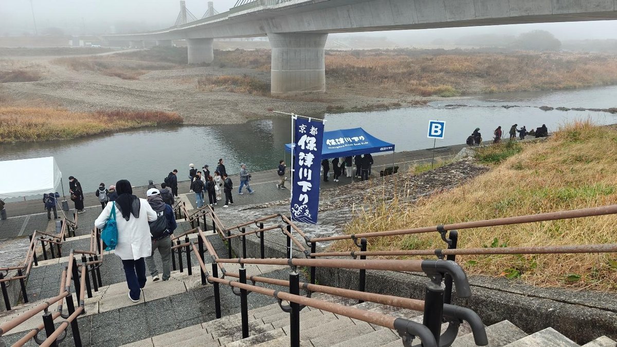 People by riverbank with bridge in foggy background