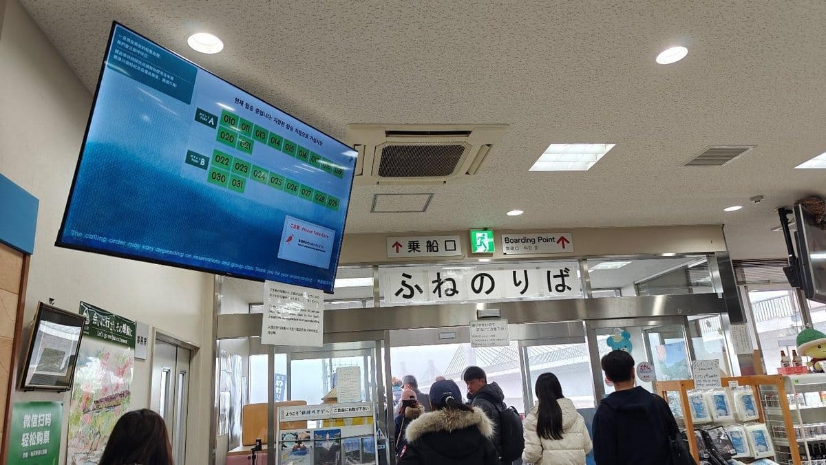 People in a ferry boarding area with digital display