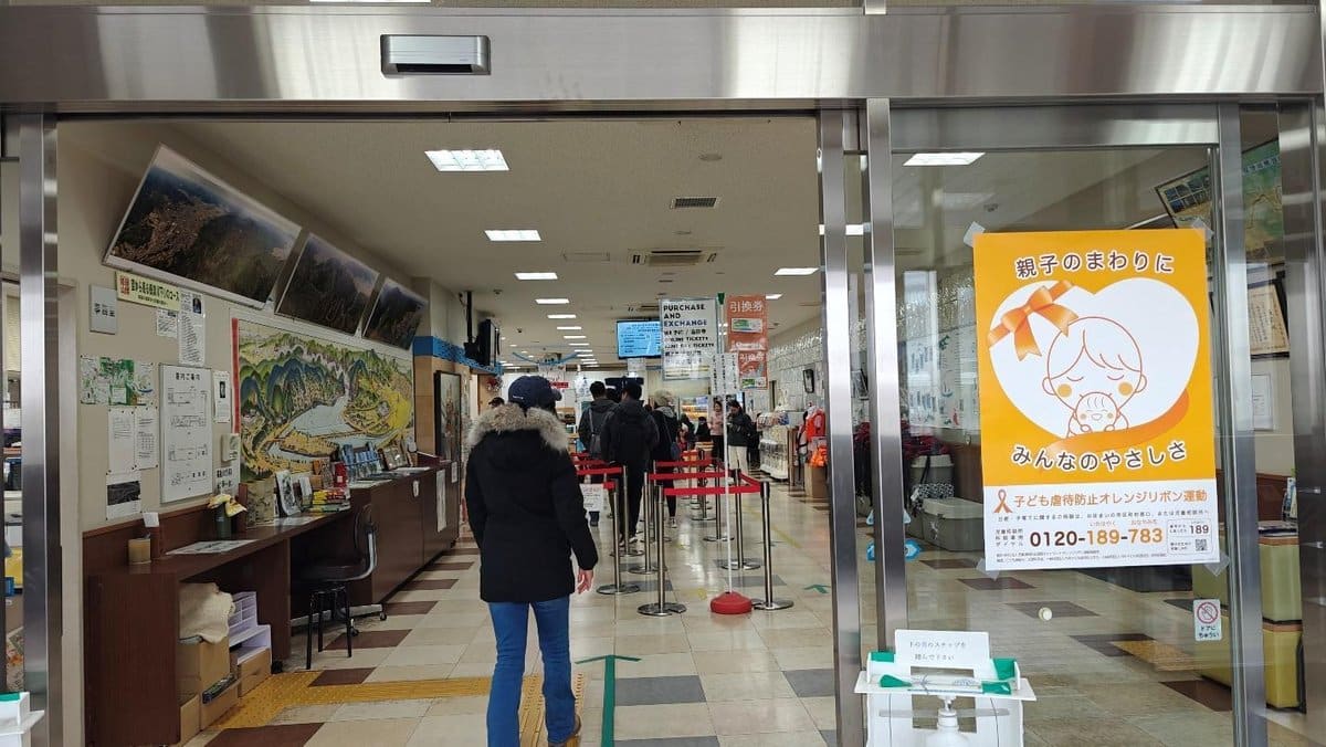 People in line inside a building with posters and maps