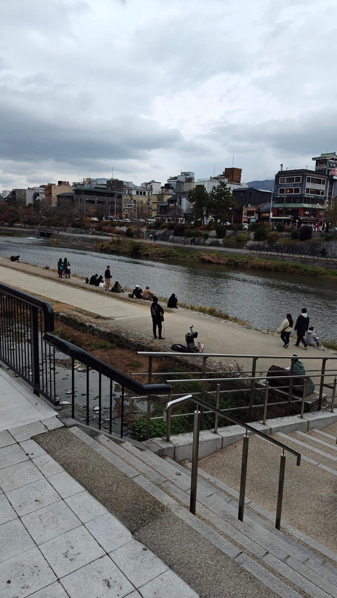 People relaxing by a river under cloudy skies