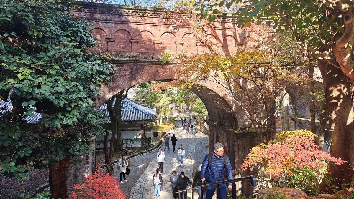 People stroll under a historic brick aqueduct in autumn scenery
