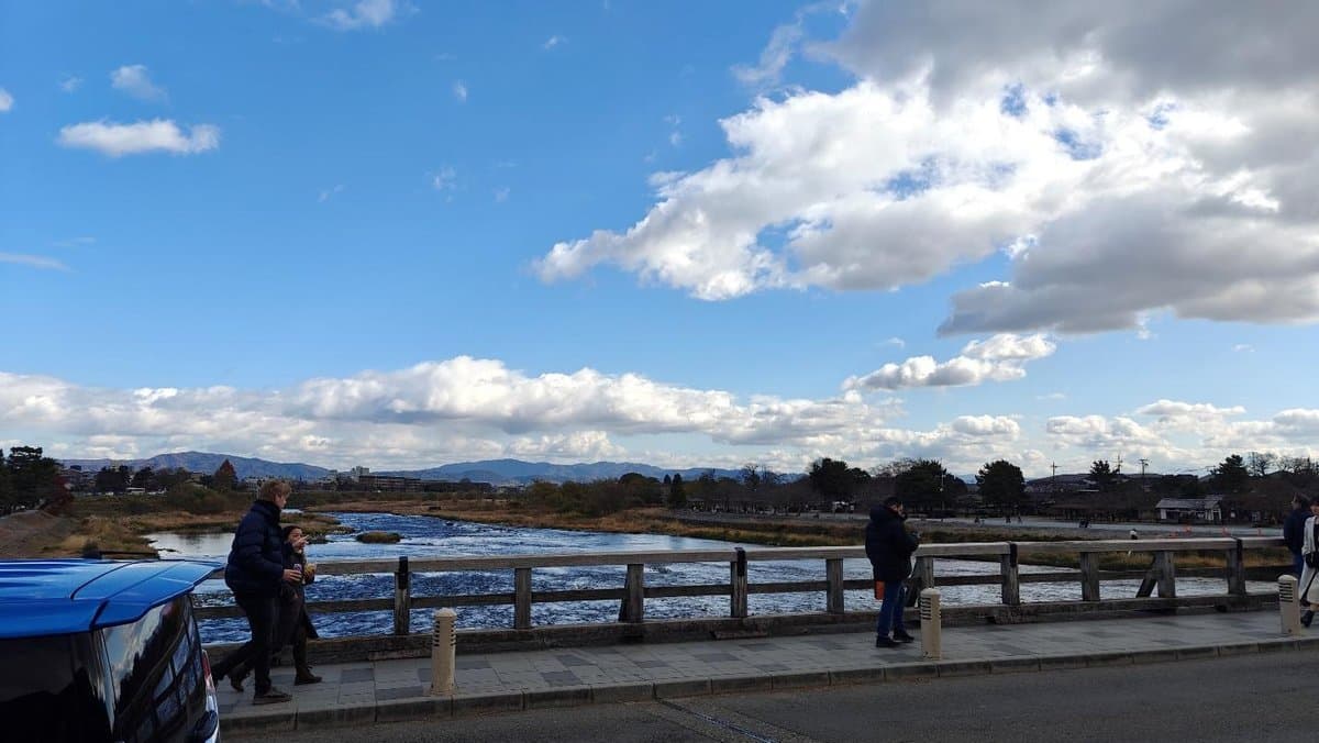 People walk along riverside under blue sky and clouds
