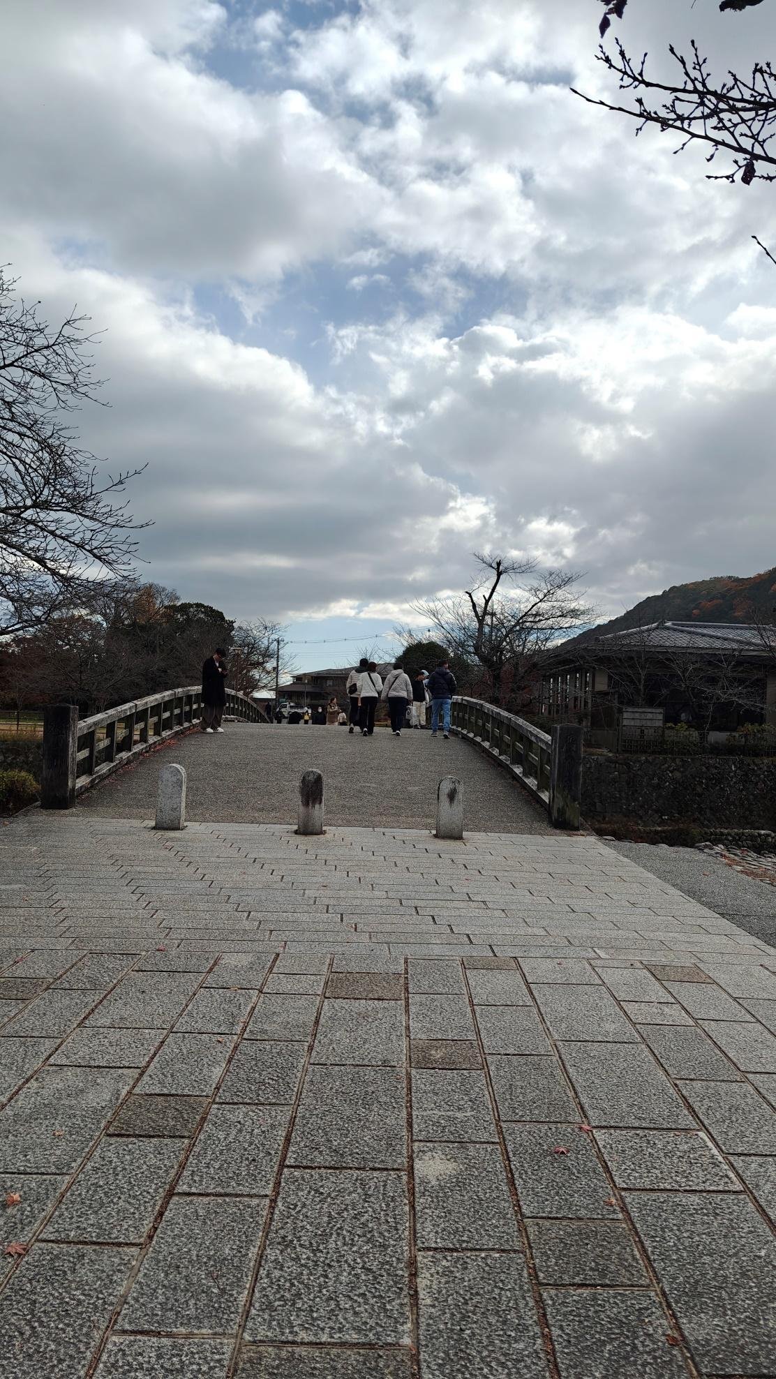 People walk on a stone bridge under cloudy sky