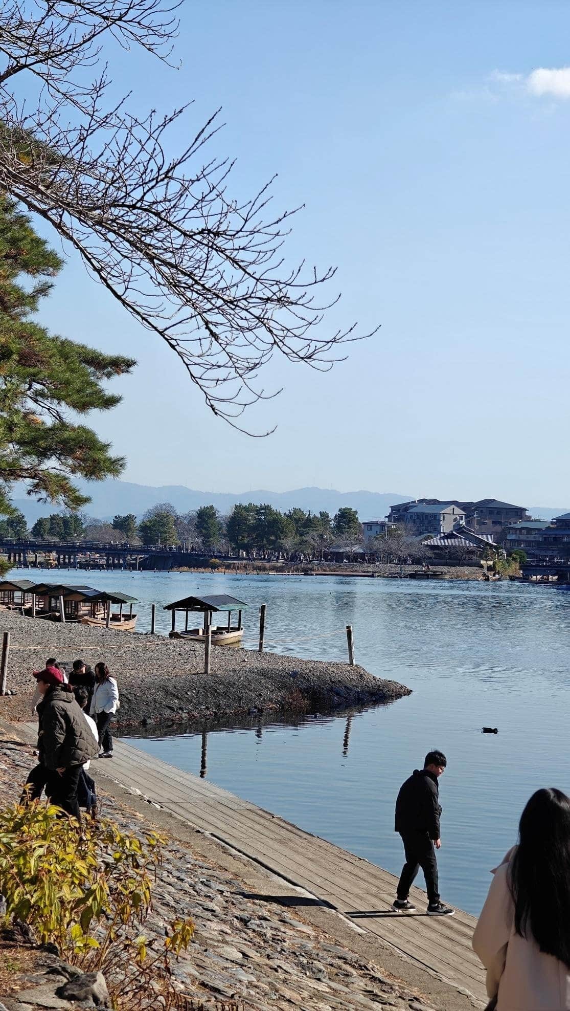 People walking by a calm lake with wooden boats and trees