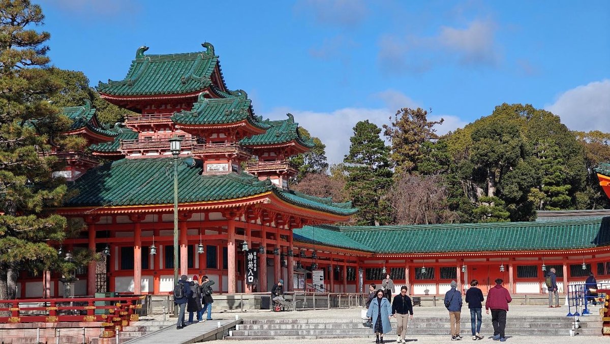 People walking by traditional Japanese temple with green roofs