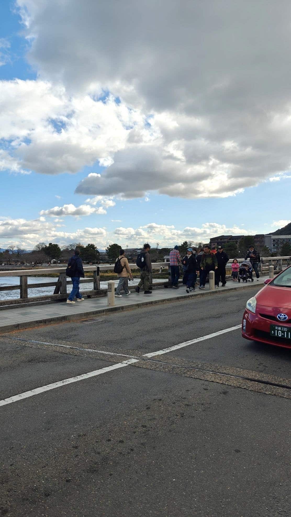 People walking on a riverside bridge under cloudy sky