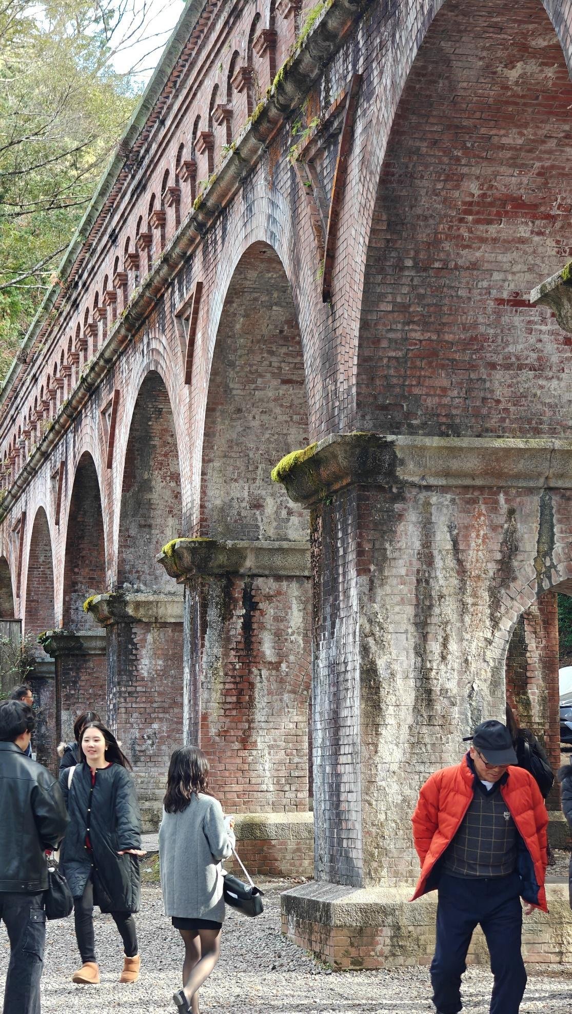 People walking under brick archway with moss-covered structures