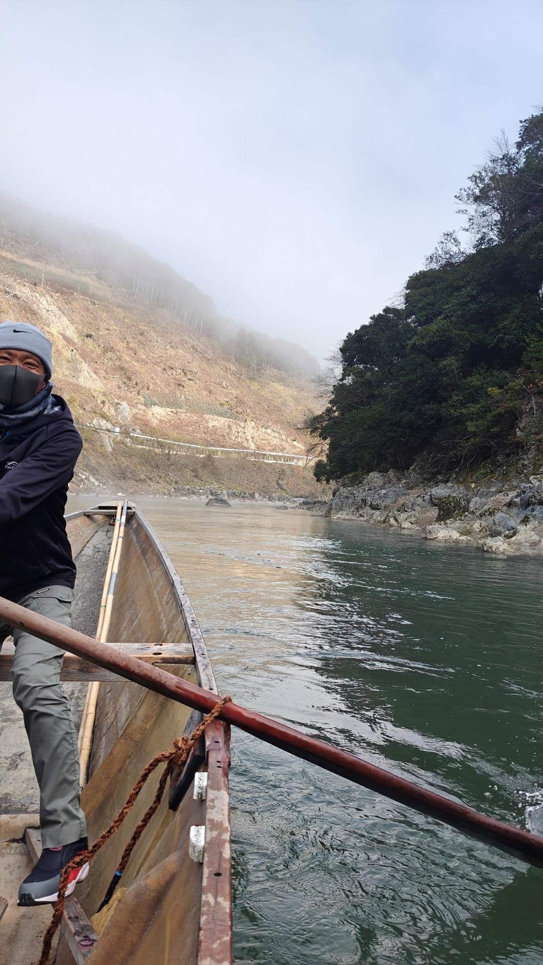 Person rowing boat on misty river, rocky landscape