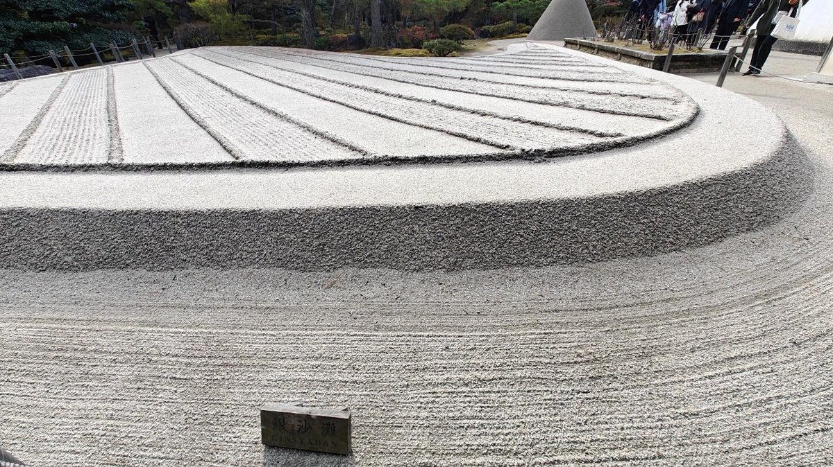 Raked sand garden with textured patterns and surrounding greenery