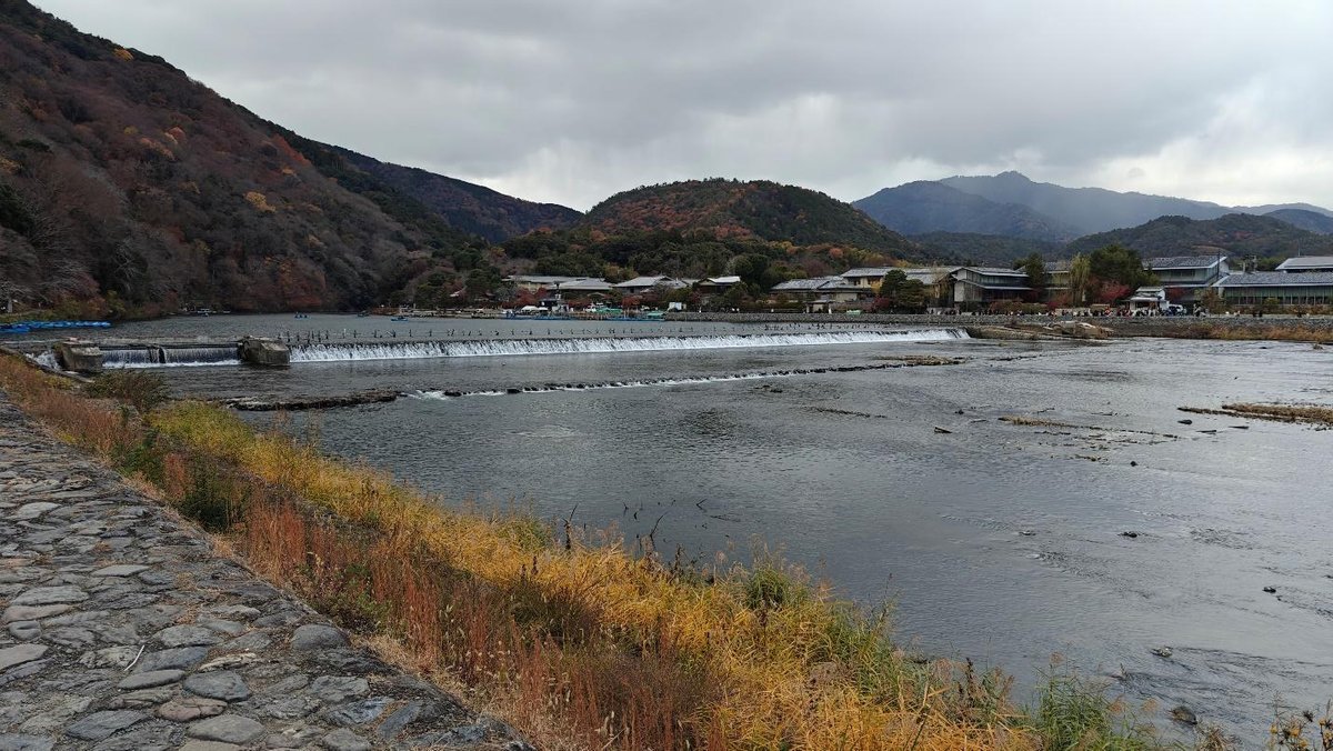 River with autumn foliage and distant village under cloudy sky