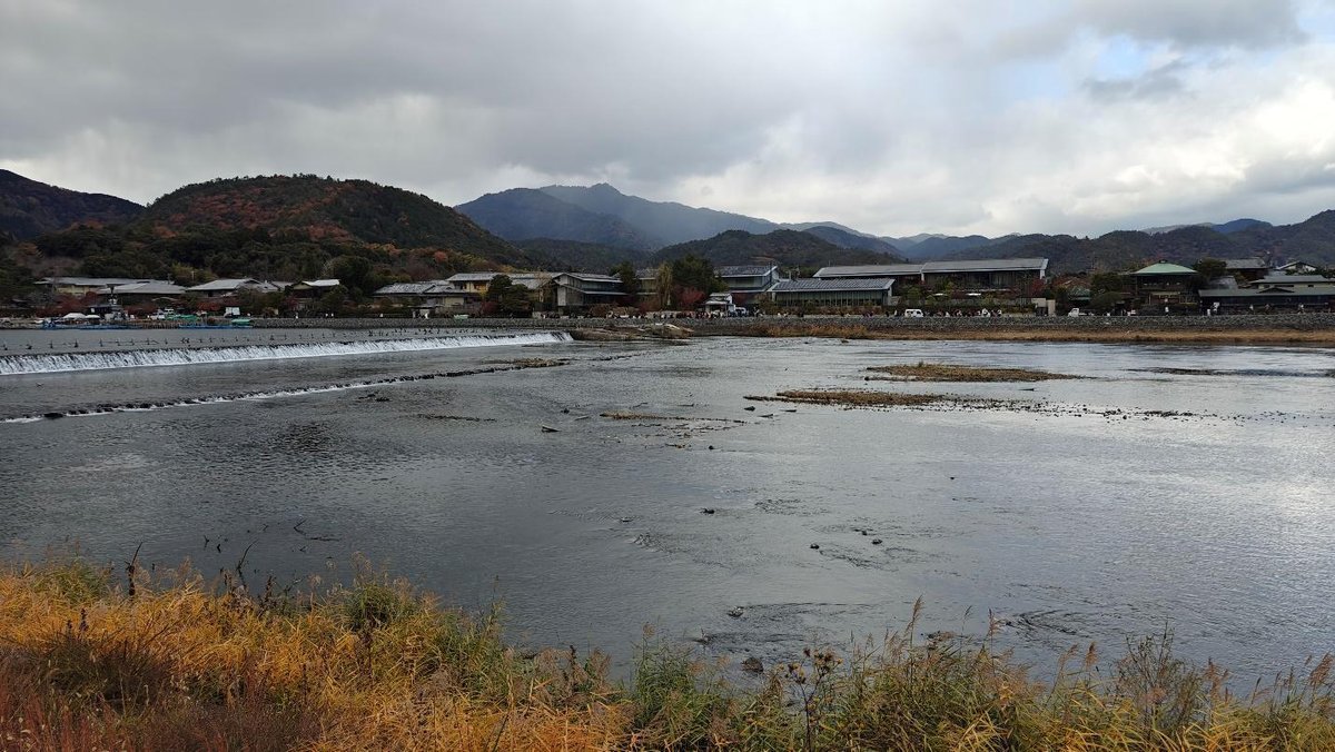 River with lush hills and village under cloudy sky