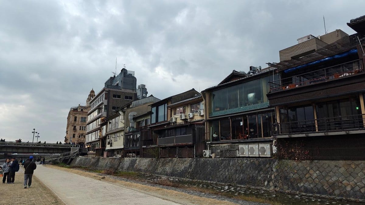 Riverside buildings under cloudy sky, people strolling