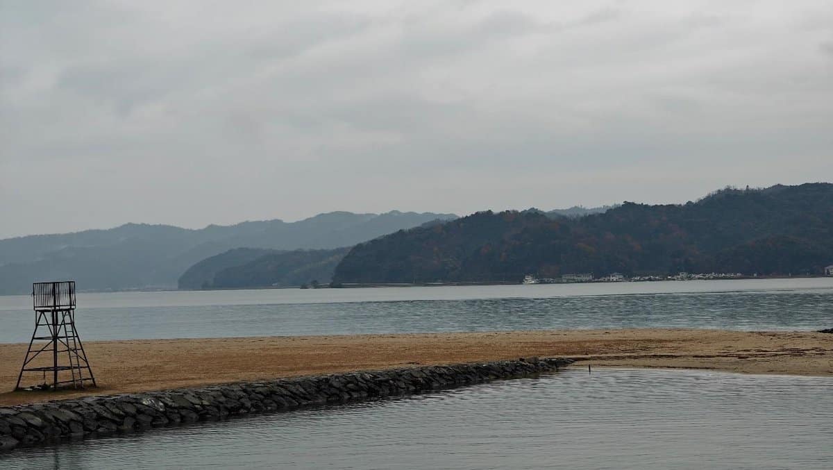 Calm beach with mountains under cloudy sky