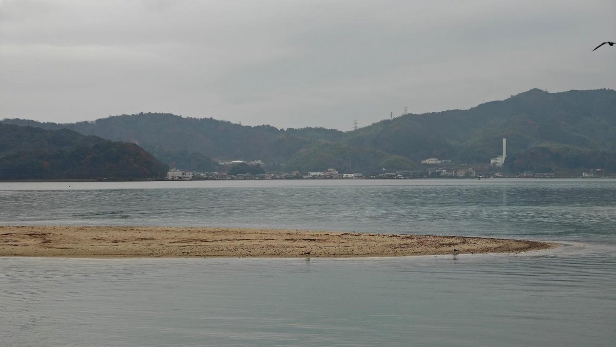 Calm waters with distant hilly landscape under cloudy sky